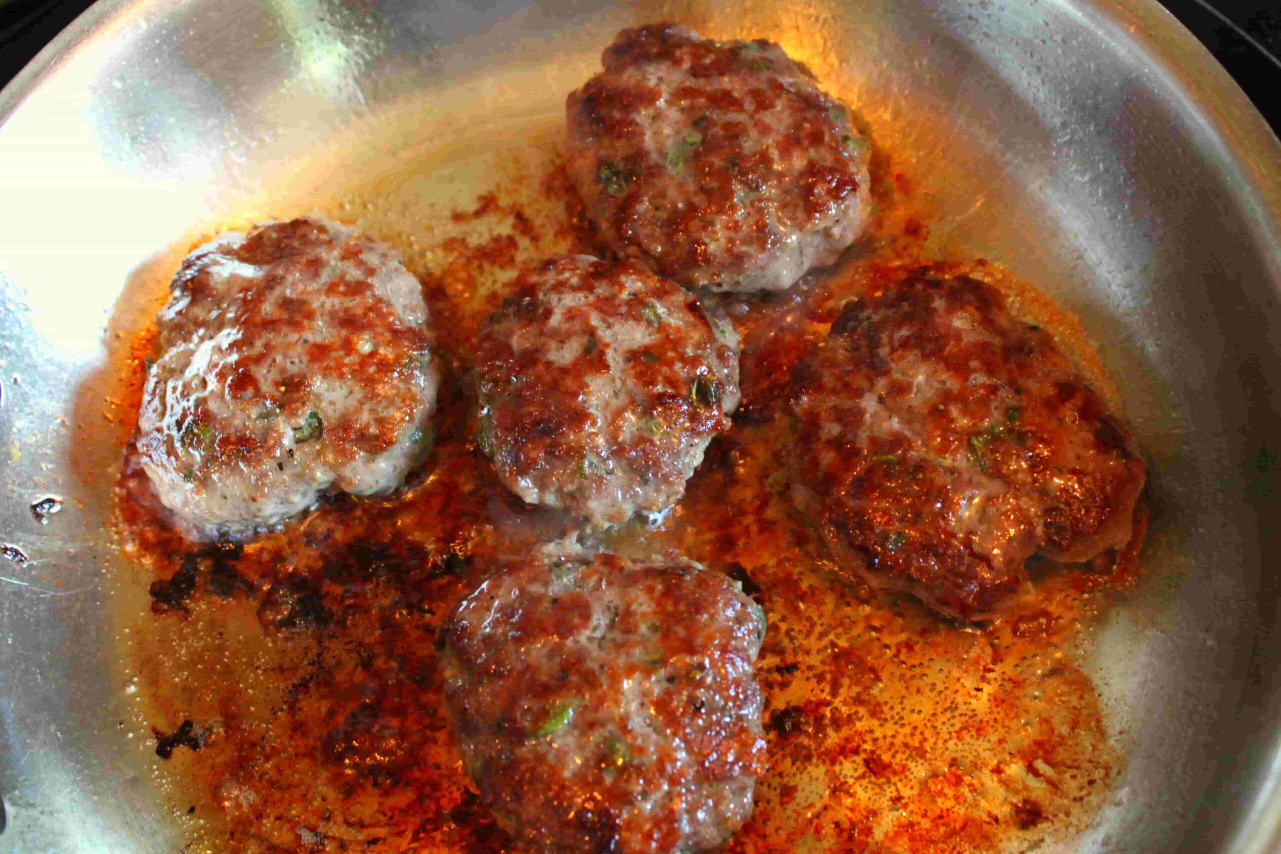 elk sausage patties cooking on pan