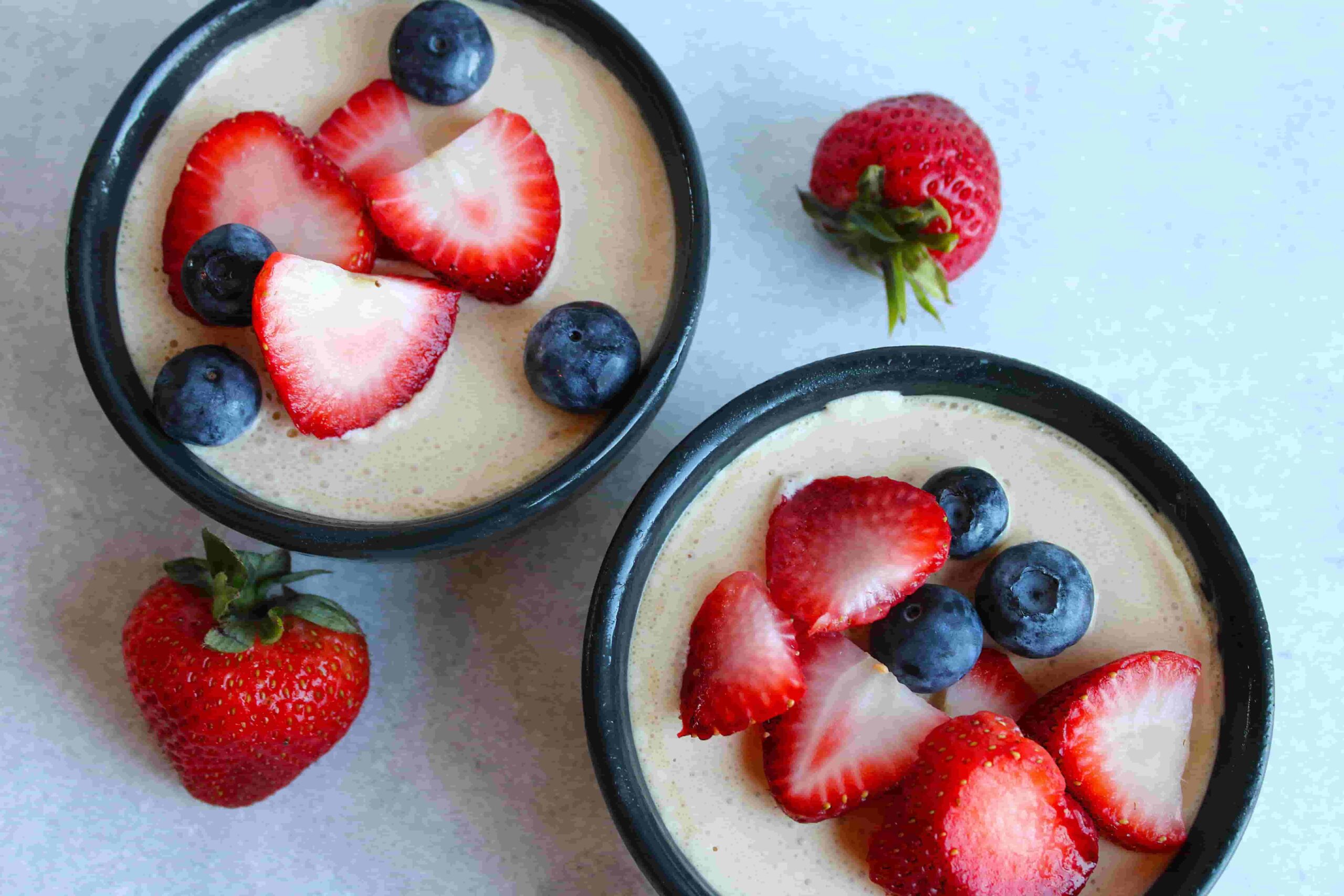 healthy no bake cheesecake in small black bowls with fresh berries on top birds eye view