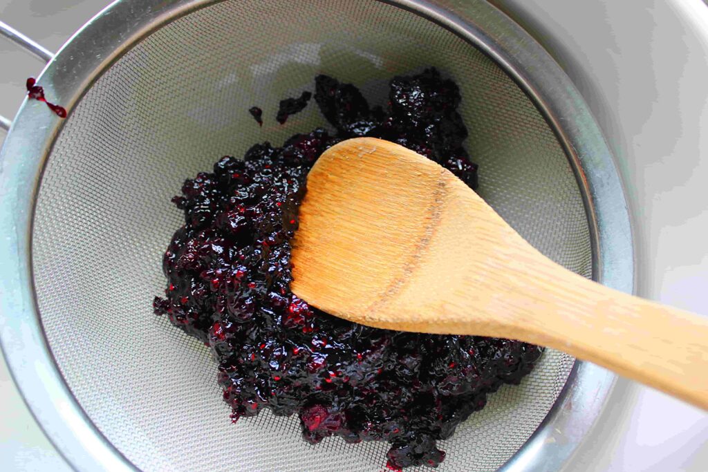 pushing homemade blackberry jam through sieve with wooden soon