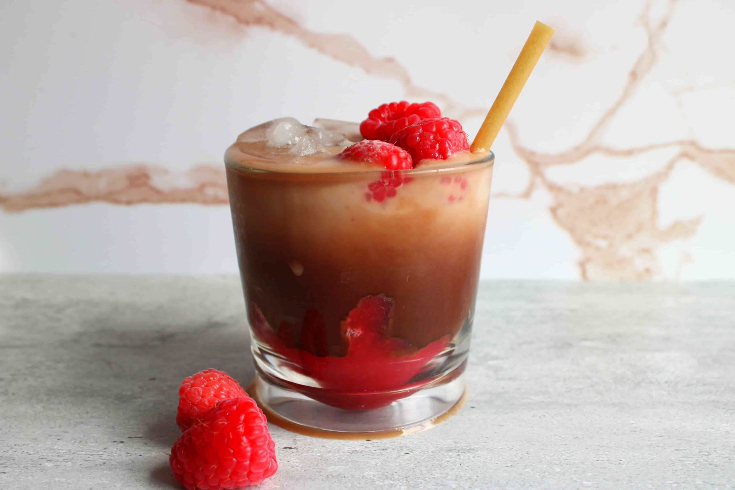raspberry mocha latte in glass with ice and fresh raspberries, with tan straw