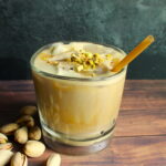 homemade pistachio latte in glass with crushed pistachios on top and pistachios next to it