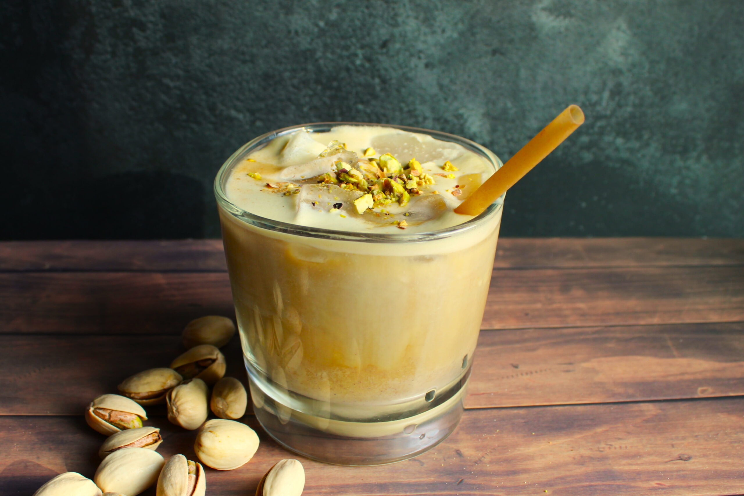 homemade pistachio latte in glass with crushed pistachios on top and pistachios next to it