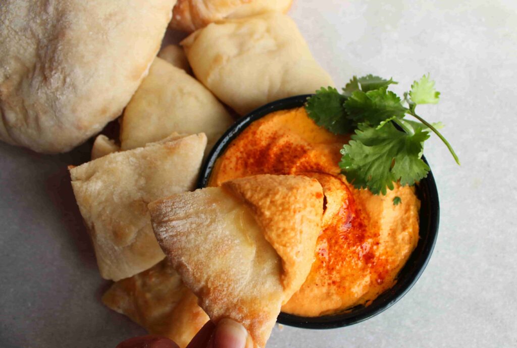 roasted red pepper hummus no tahini with pita bread on side and pita being dipped in